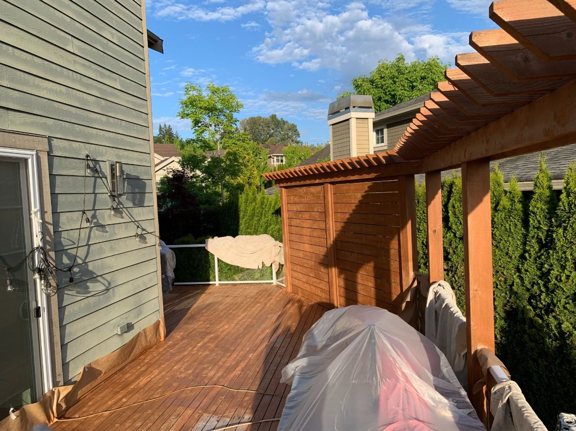 Deck staining Redmond WA — cedar deck and pergola being restained with drop cloths protecting furniture