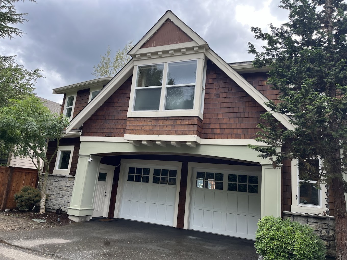 Exterior house painting Redmond WA — craftsman home with rich cedar shake siding, sage green trim and white carriage garage doors