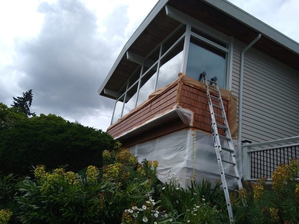 Exterior painting Redmond WA — cedar shake dormer masked off and prepped with ladder mid-repaint