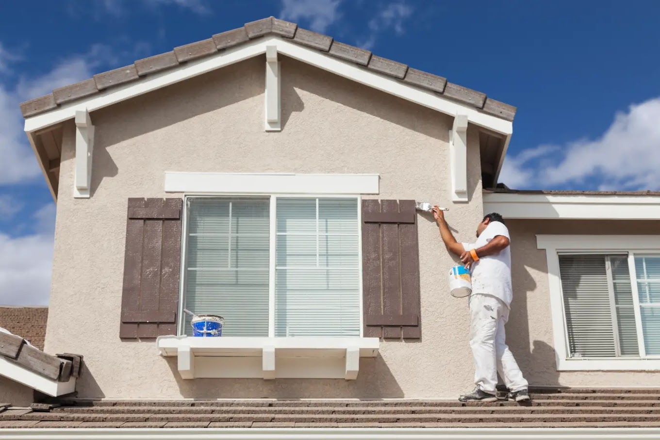 Exterior house painter Redmond WA — Redmond Pro Painting crew member brush-painting brown shutters on a stucco home