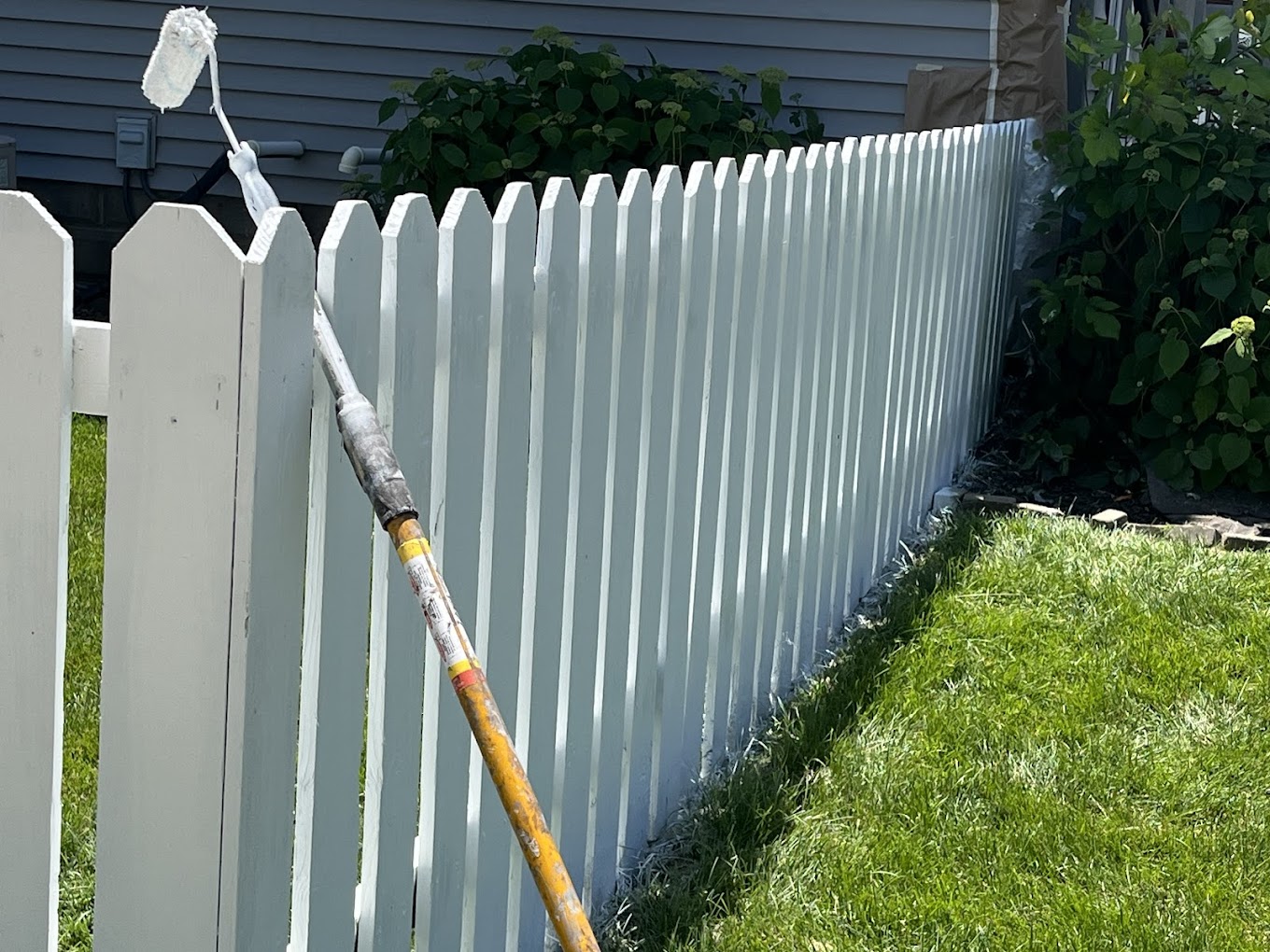 Fence painting Redmond WA — fresh white paint being rolled onto a picket fence in a sunny backyard