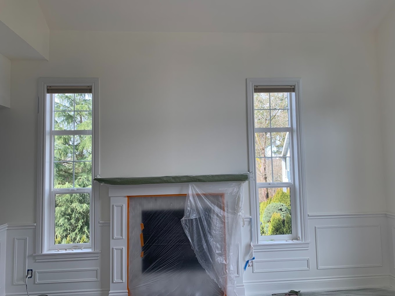 Interior painting Redmond WA — living room with white wainscoting and fireplace masked off for repaint